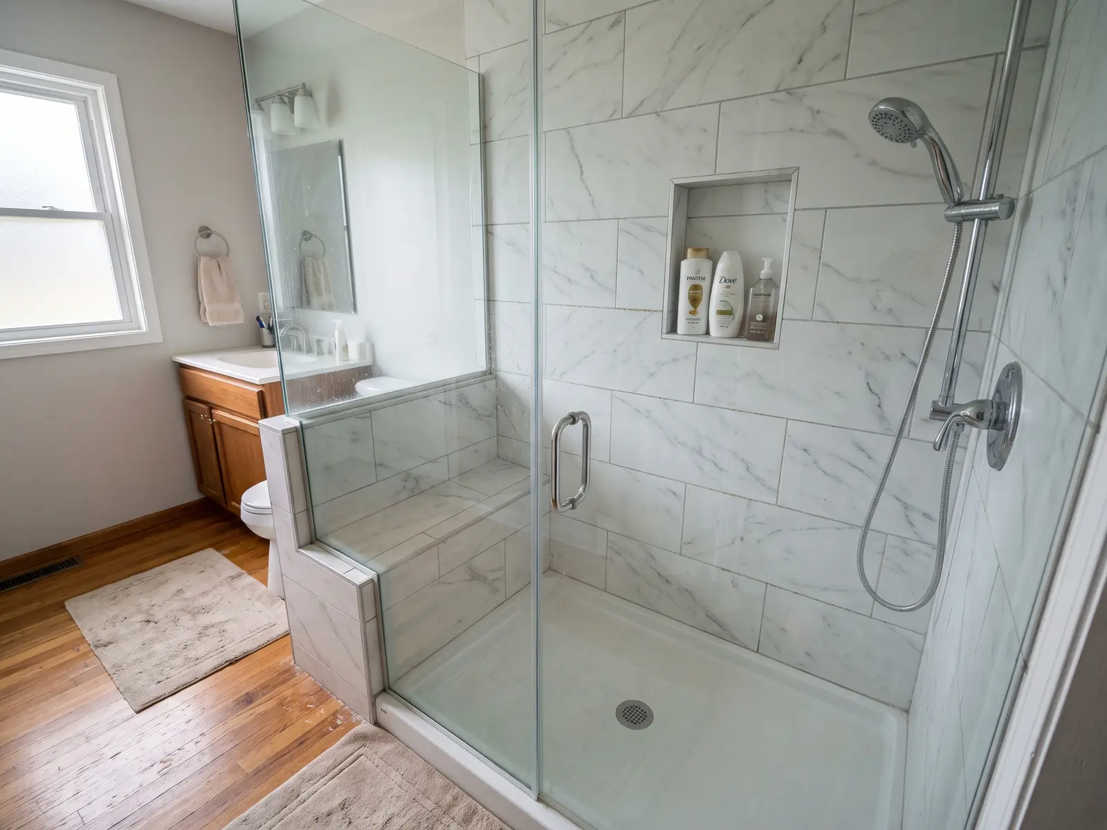Walk-in shower with a low threshold, frameless glass door, built-in bench and marble-look tile